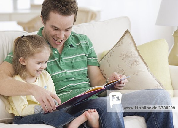 Father reading to daughter on sofa