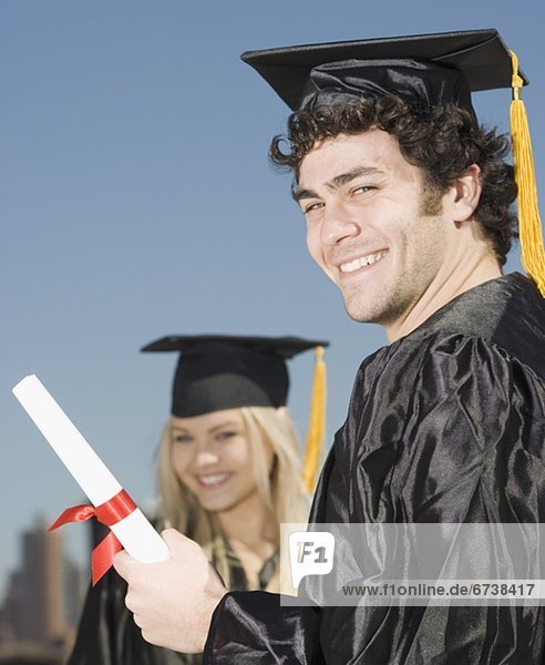 Man wearing graduation cap and gown with diploma
