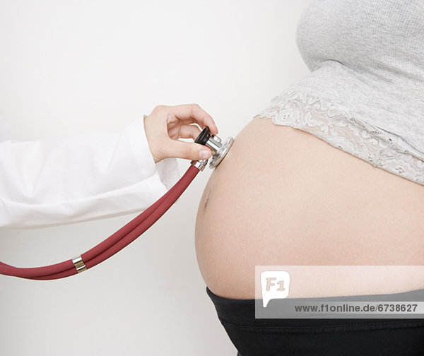 Doctor holding stethoscope on pregnant womanÕs belly
