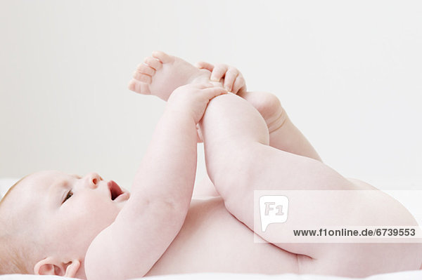 Naked baby laying on back and grabbing feet