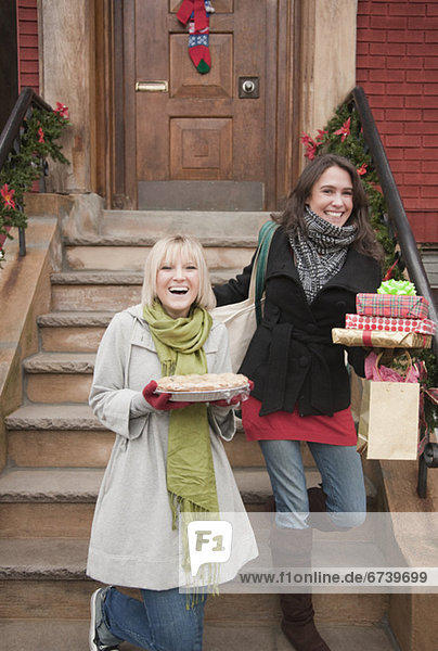 Women carrying Christmas gifts on front stoop