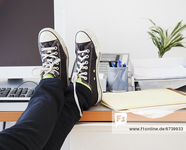 Young office worker in casual clothes relaxing in office with legs on desk