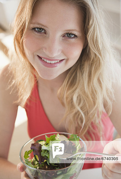 Junge Frau isst stehend einen Salat