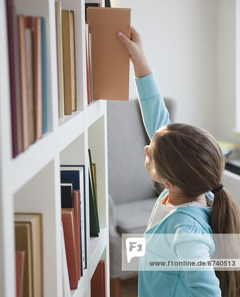 Young girl taking book of bookshelf