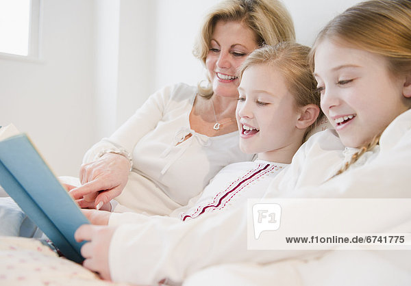 USA  Jersey City  New Jersey  mother and daughters (8-11) reading book in bed