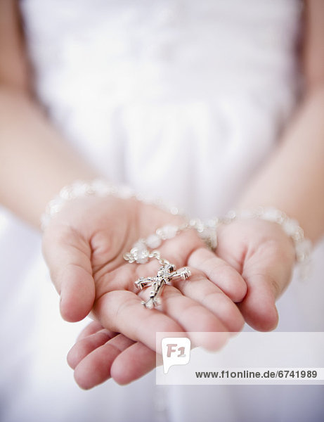 Close up of girl's (8-9) hands holding rosary beads