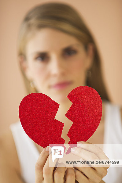 Young woman holding broken paper heart