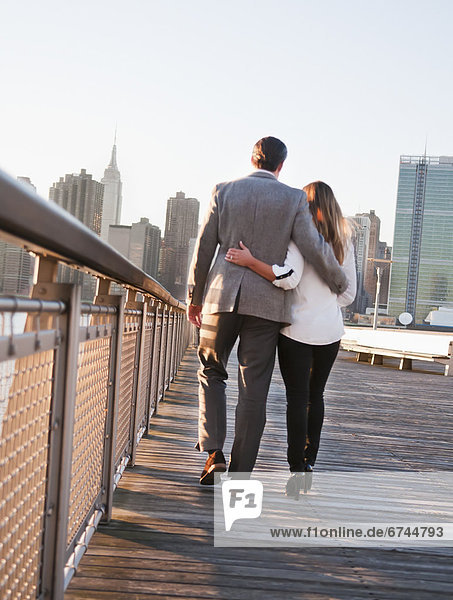 USA  New York  Long Island City  Rear view of young couple walking on boardwalk  Manhattan skyline in background