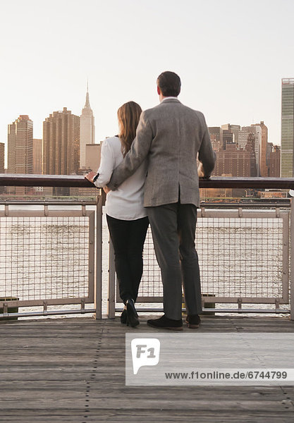 USA  New York  Long Island City  Rear view of young couple standing on boardwalk  Manhattan skyline in background