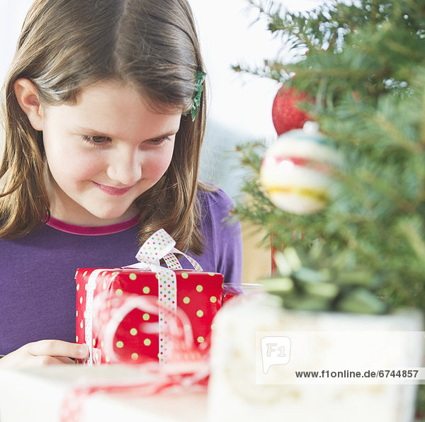 Girl (8-9) standing with gift behind Christmas tree