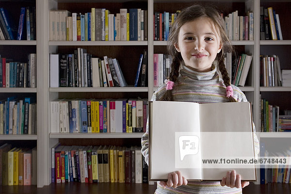 Young Girl Holding Book in front of Library Shelf