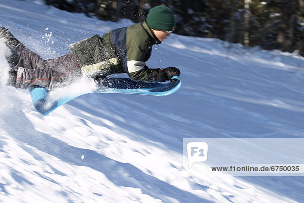 Boy in Mid-Air Sliding Down Snow Covered Hill
