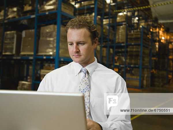 Businessman looking at laptop in warehouse