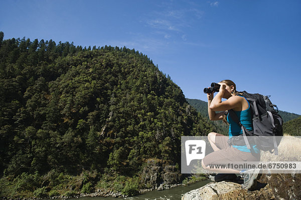 Hiker looking through binoculars on river overlook