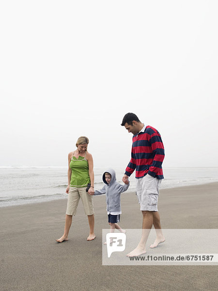 Parents holding hands with son on beach