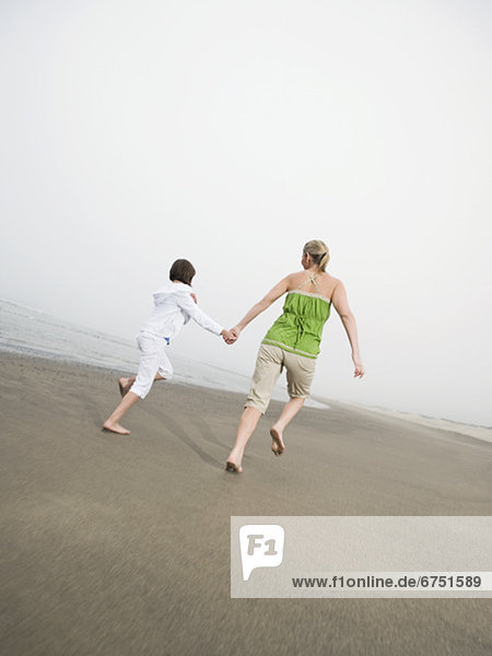 Mother and daughter holding hands and running on beach