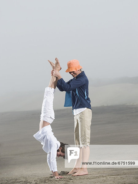 Mother holding daughter upside down on beach