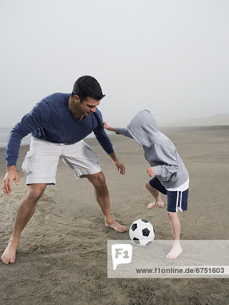 Father and son playing soccer on beach