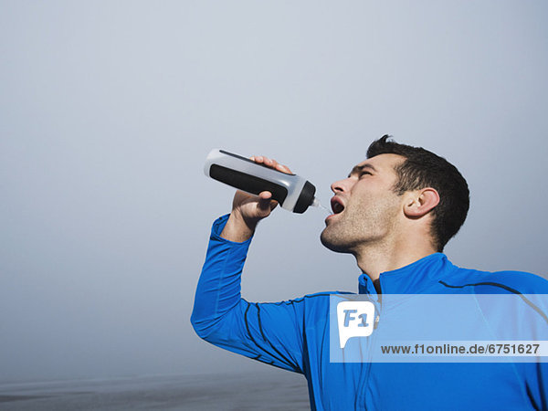Man drinking from water bottle on foggy beach