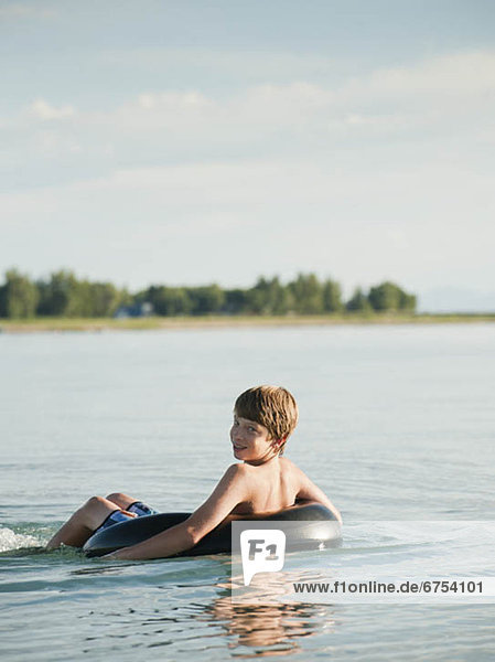 Boy (12-13) floating on rubber ring on lake