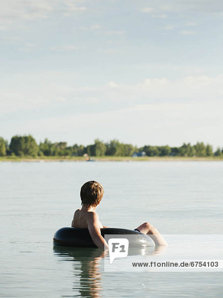 Boy (12-13) floating on rubber ring on lake