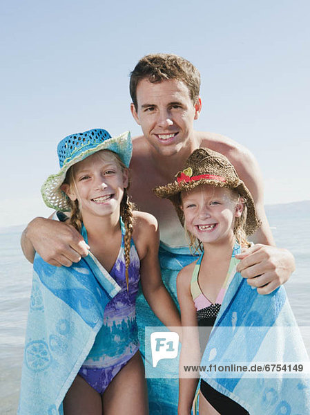 Portrait of girls (6-7 8-9) wrapped in towel on beach with their father