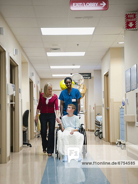 Nurse and mother walking behind boy's (10-11) wheelchair
