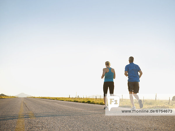 Mid adult couple running on empty road