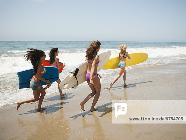 Group of young attractive women running into water with surfboards