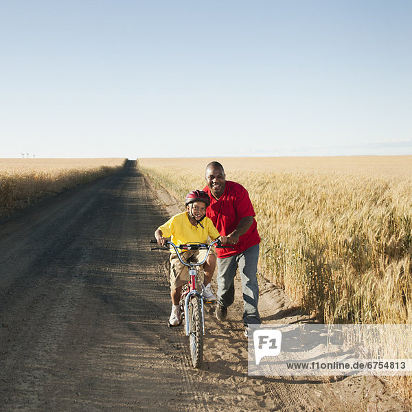Father teaching son (8-9) how to cycle on along dirt road
