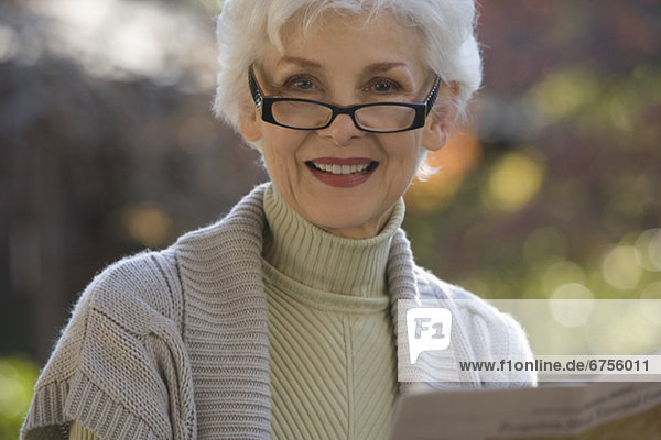 Portrait of senior woman reading newspaper outdoors