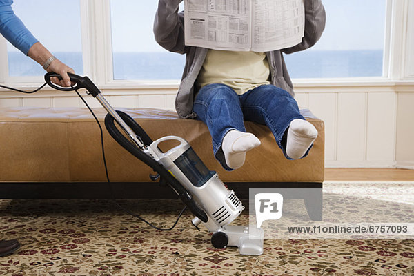 Woman vacuuming under manÕs feet