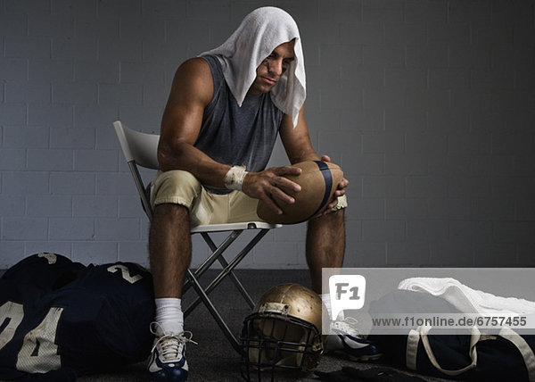 Football player with towel on head in locker room