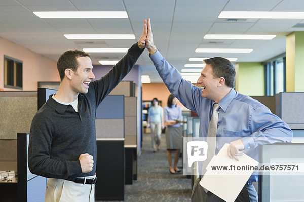 Businessmen high-fiving in office