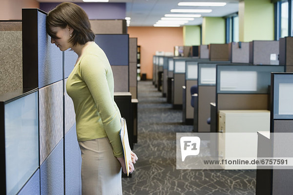 Businesswoman leaning head on cubicle wall