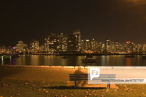 Transparent man on bench and city lights at night  False Creek  Vancouver  British Columbia