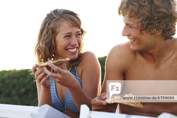 Young couple eating pizza at beach