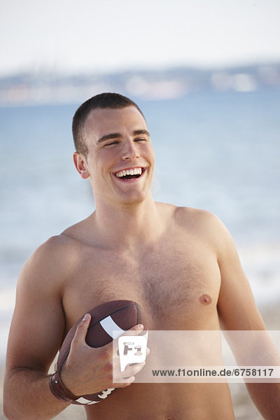Young man holding football on beach
