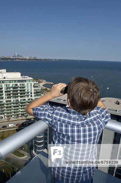 Young Boy Looking at City Skyline through Binoculars from a Condo Rooftop  Toronto  Ontario