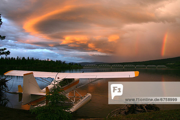 Sunlit Storm Clouds over a Float Plane with Rainbow and Teslin bridge in background  Teslin Lake  Yukon