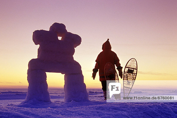 Man in a Parka Standing beside Snowshoes and an Inukshuk  along Lake Winnipeg  Manitoba