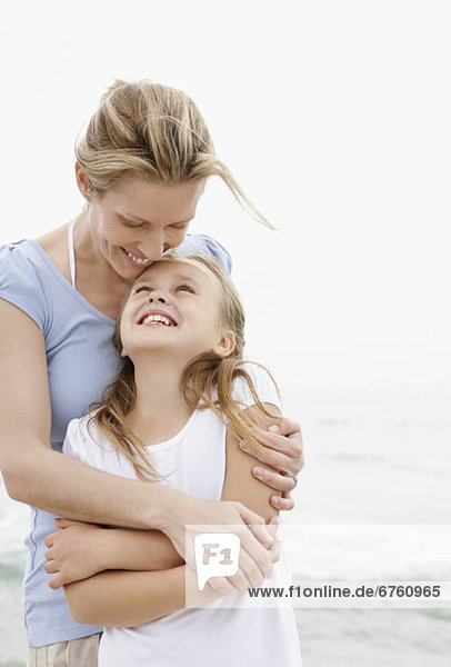 Mother with embracing daughter (10-11) on beach