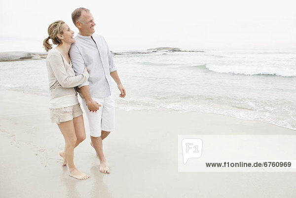 Couple holding hands and walking on empty beach