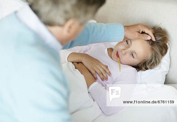 Grandfather tending granddaughter (10-11) lying in bed with thermometer in mouth