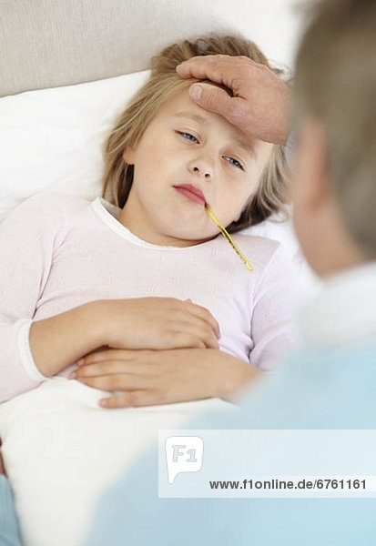 Grandfather tending granddaughter (10-11) lying in bed with thermometer in mouth