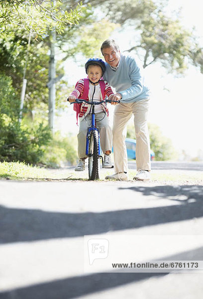 Grandfather helping granddaughter (10-11) riding bike