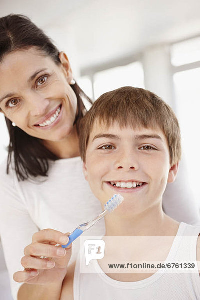 Mother embracing son (12-13) while he is brushing teeth