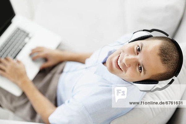 South Africa  Young man wearing headphones sitting on sofa and using laptop  high angle view