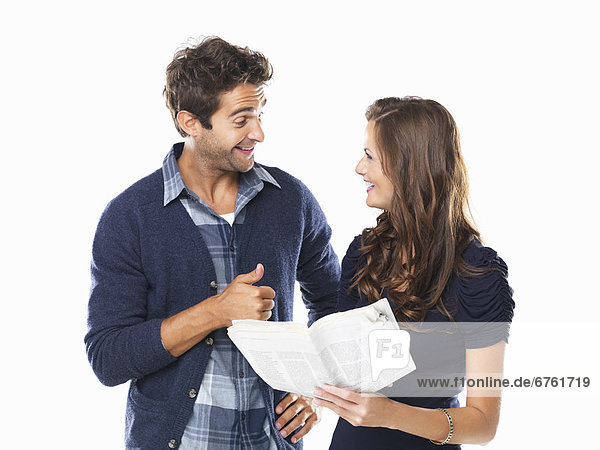Studio shot of young couple with newspaper smiling and looking at each other