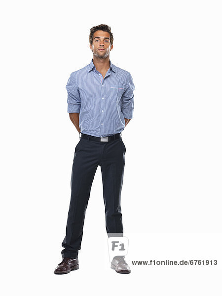 Studio shot of young business man standing with hands behind back